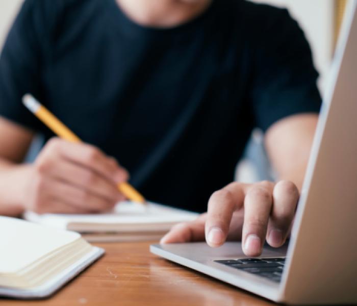 Person sitting at desk writing and using a laptop image