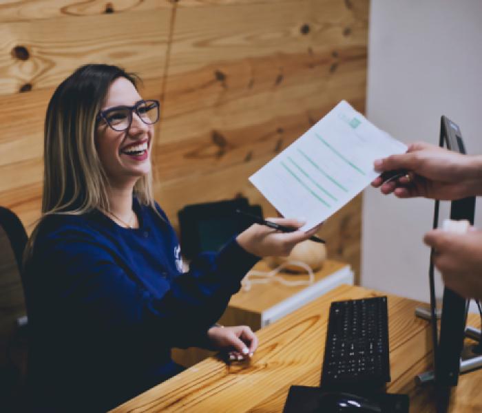 Person handing a women behind a desk a paper image