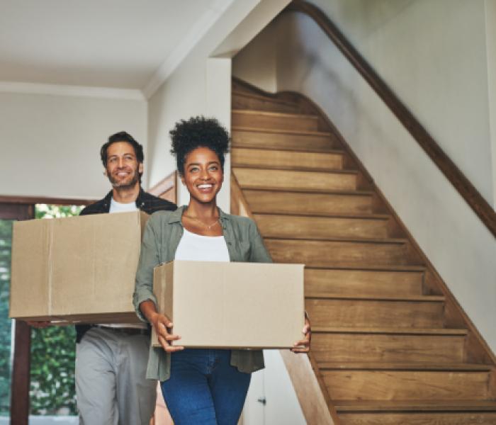 Two people moving, carrying boxes within a house image