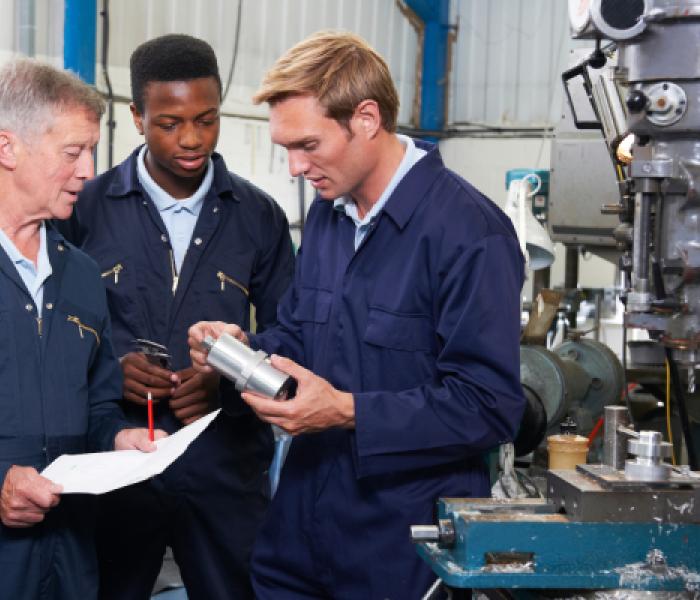 Factory workers examining a part next to machinery equipment